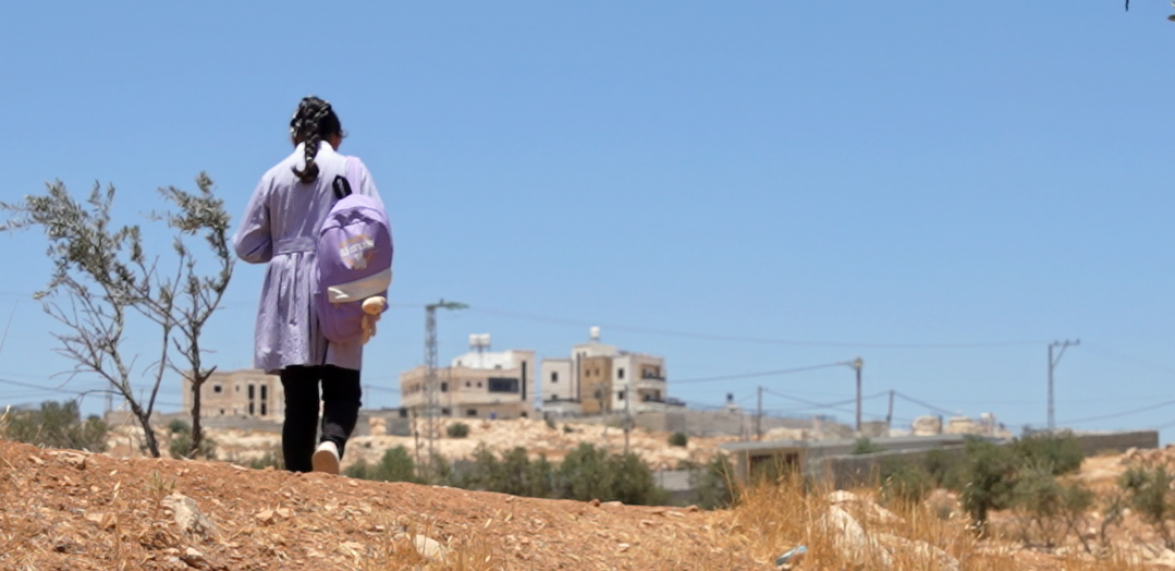 Mona*, 12, walks to school with her school bag on her back