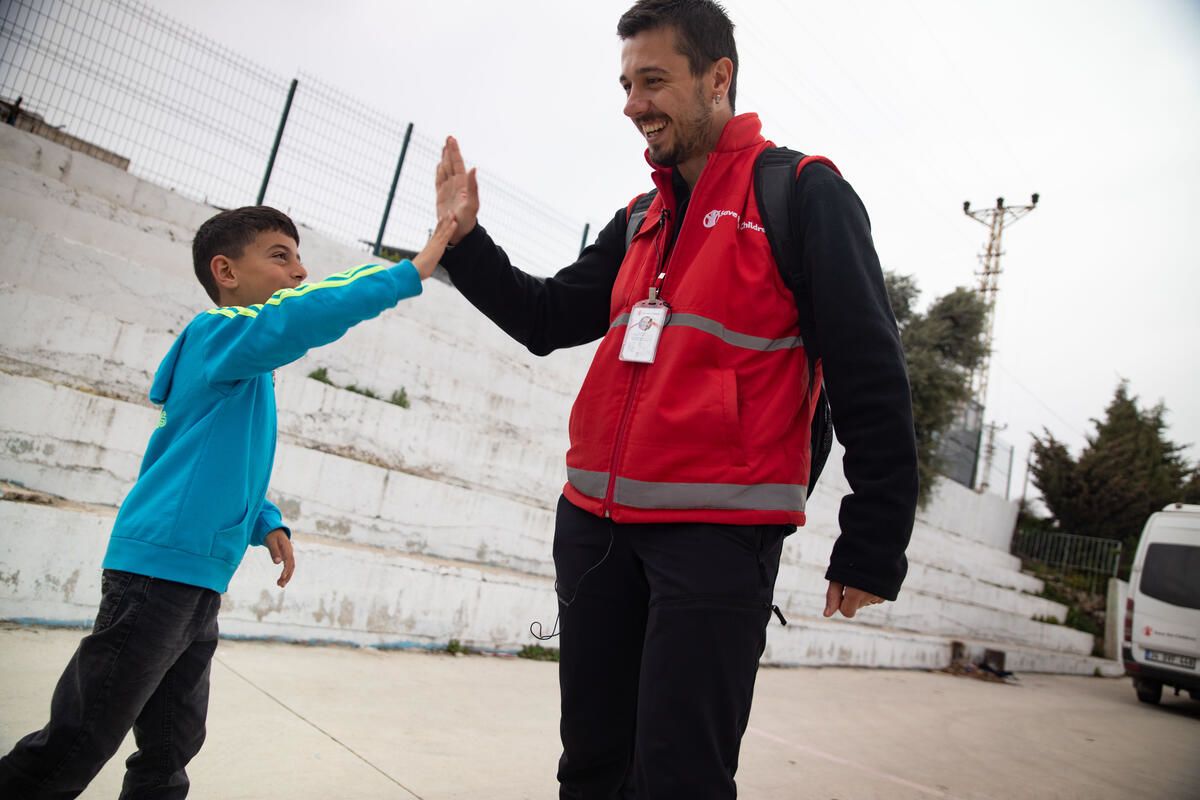 Photo: Save the Children staff member, Arif, speaks and plays with Umut* as part of his mental health and psychosocial support, Türkiye. They give each other a high five. Credit: Save the Children.