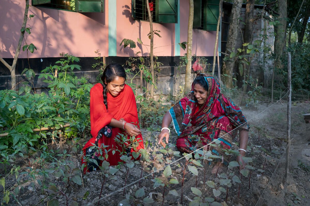 Photo: Mukta, 19, wearing a red sari, tends to her vegetable garden with her mother, Minati, at their home in Bangladesh. Credit: Fabeha Monir/Save the Children.
