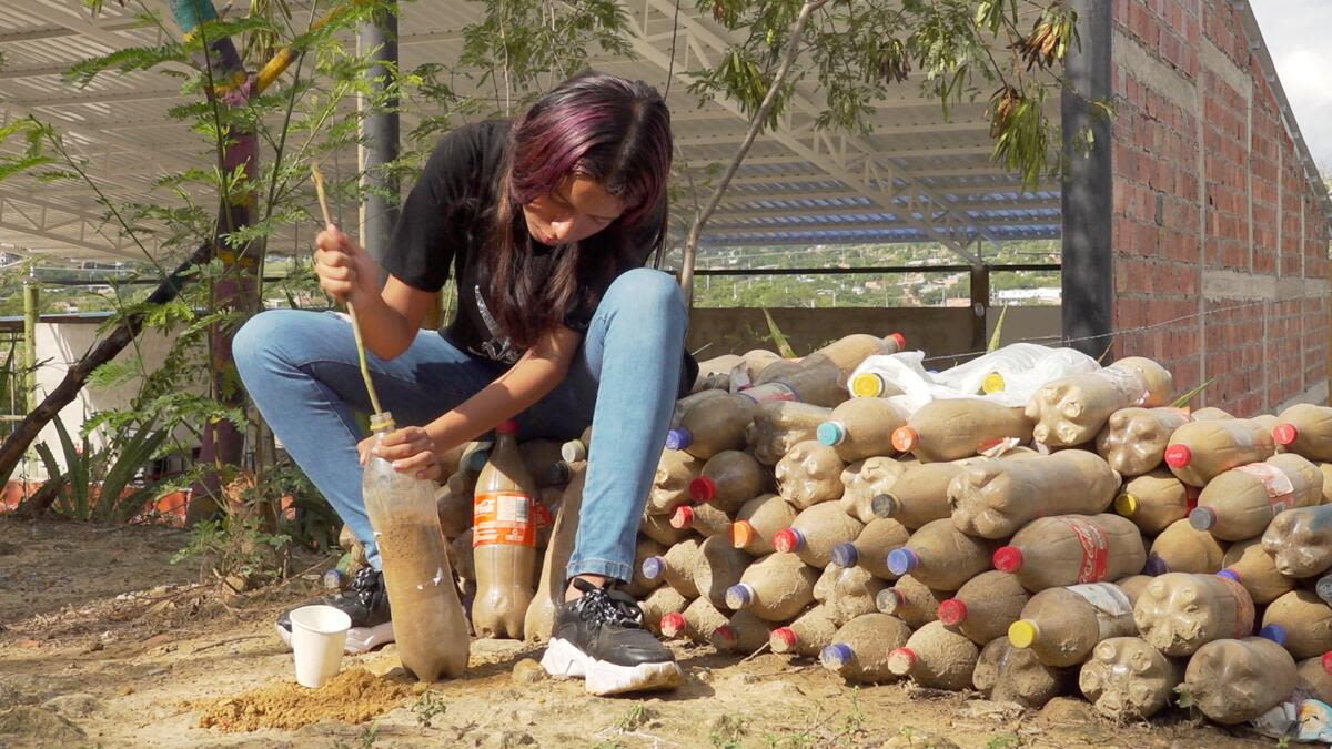 Oriana fills a plastic bottle with sand so it can be recycled as a brick.