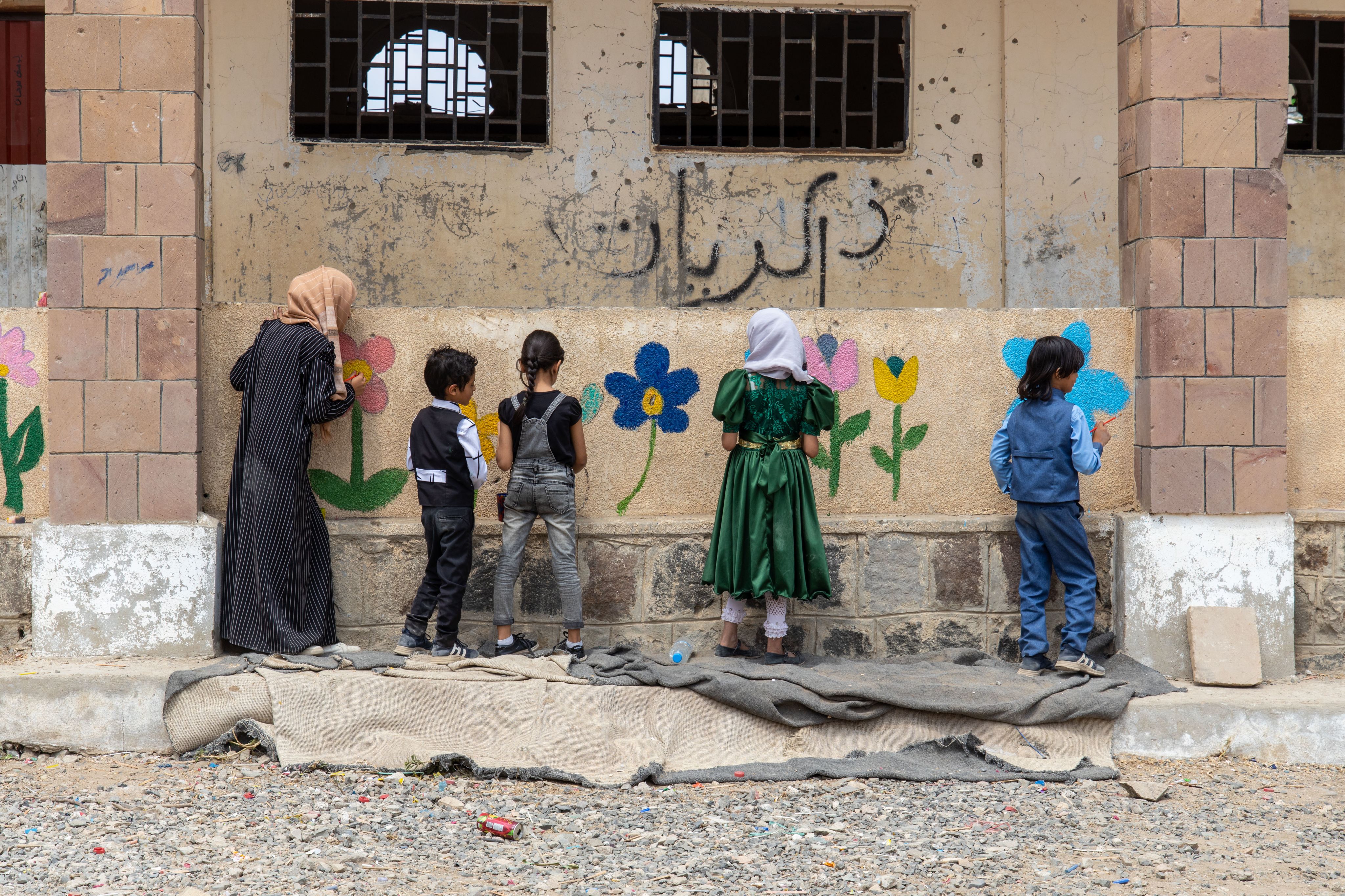 Children in Yemen paint a flower mural on the walls of a destroyed school as part of the Flowers for Children campaign