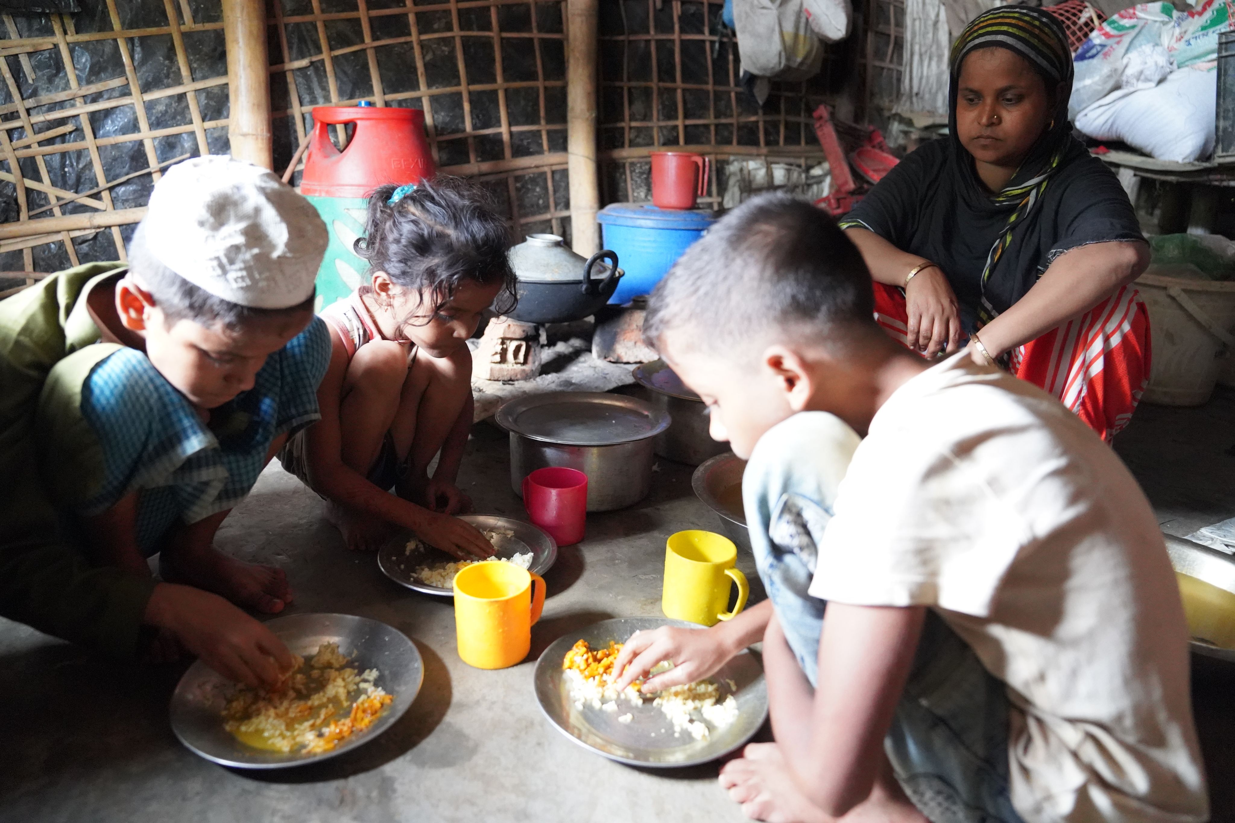 Meherun Nesa*, 40, watches her children - Antora*, 5, Zia*, 12, & Forkan*, 15 - eat a rice-based meal in Cox's Bazar, Bangladesh.