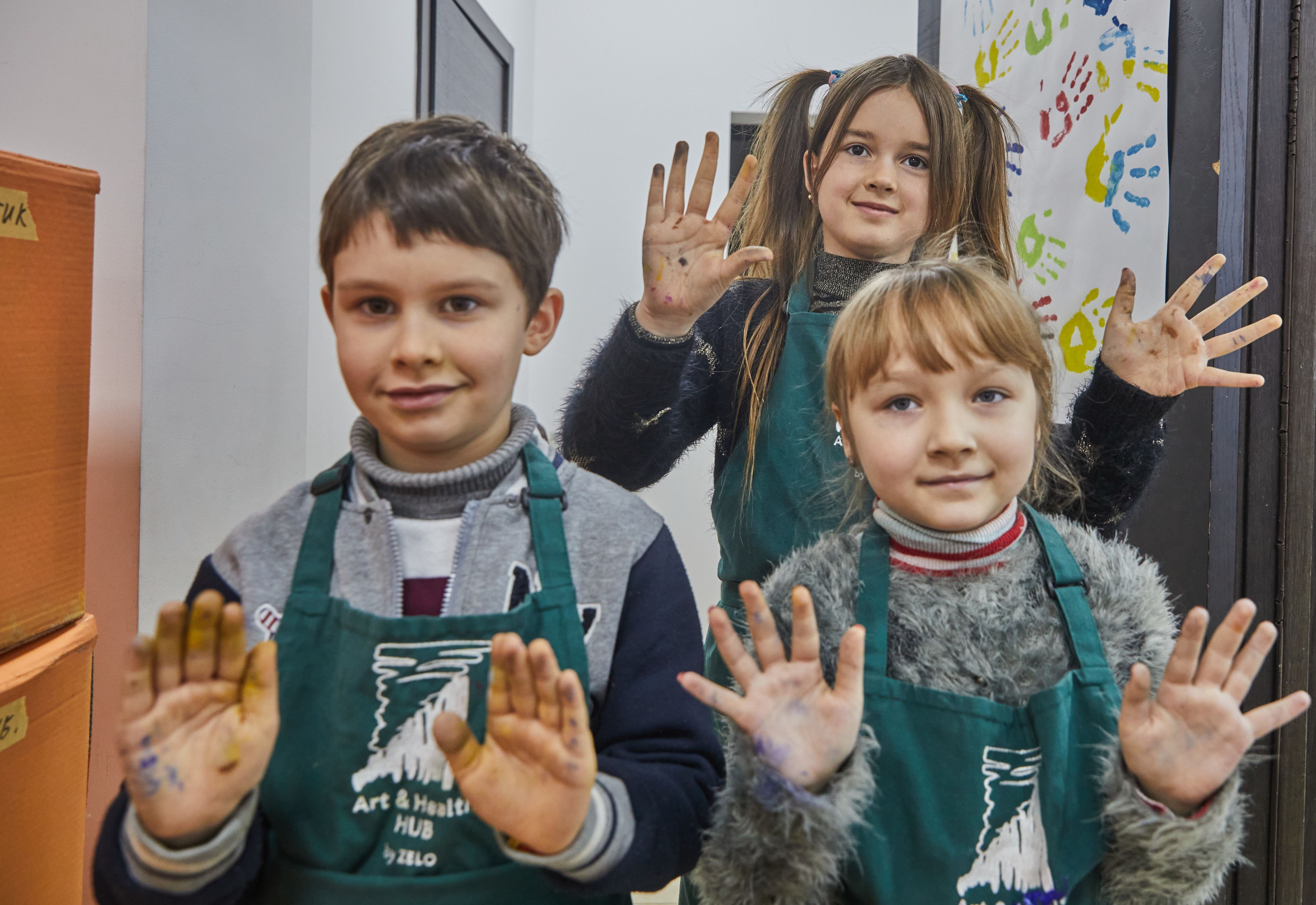 Ihor*, 7, Valentyna*, 9, and Olha*, 7, showing their hands covered in paint after an art therapy workshop in Poltava, Ukraine