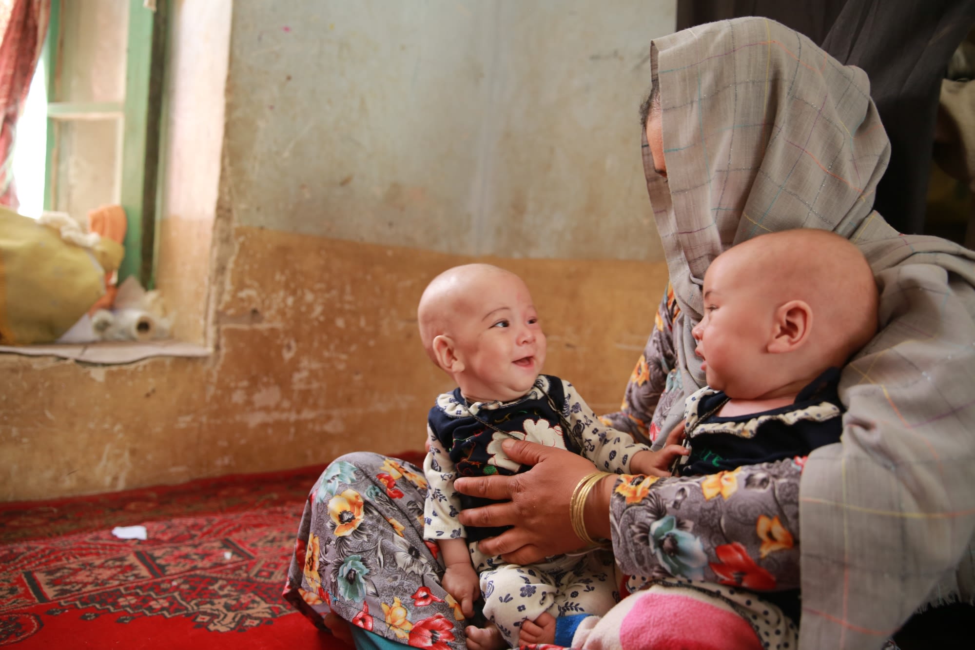 Sajida* (31), holding her twin children Nadira* and Nahida* (8 months) at her house