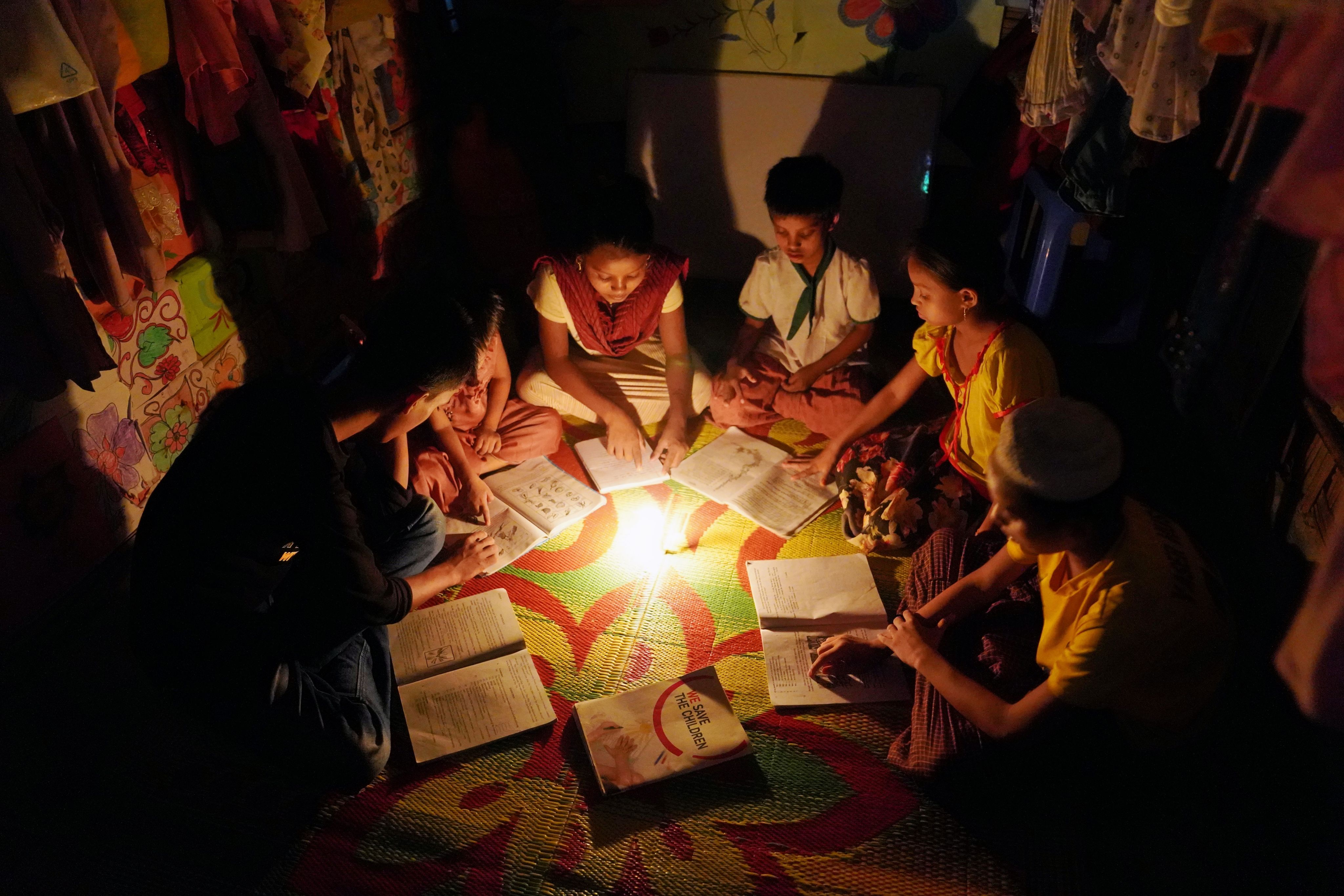 Ayaz*, 15, and his five younger siblings read by candle light in their house in Cox's Bazar, Bangladesh