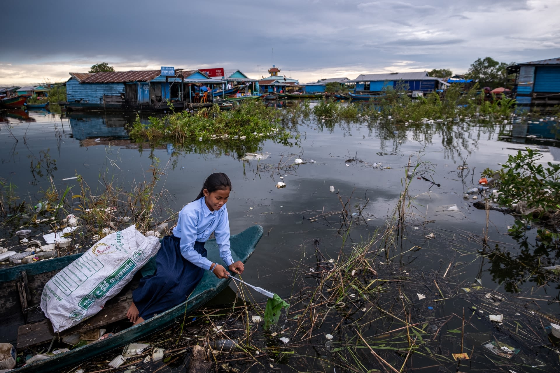 Ratana, 12, leans out of her boat to collect rubbish from Tonle Sap Lake, Cambodia.