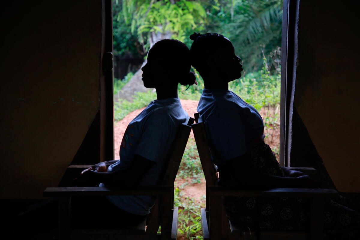 Cousins Kuji*, 19 and Kpemeh*, 18, sit back to back in Kailahun, Sierra Leone