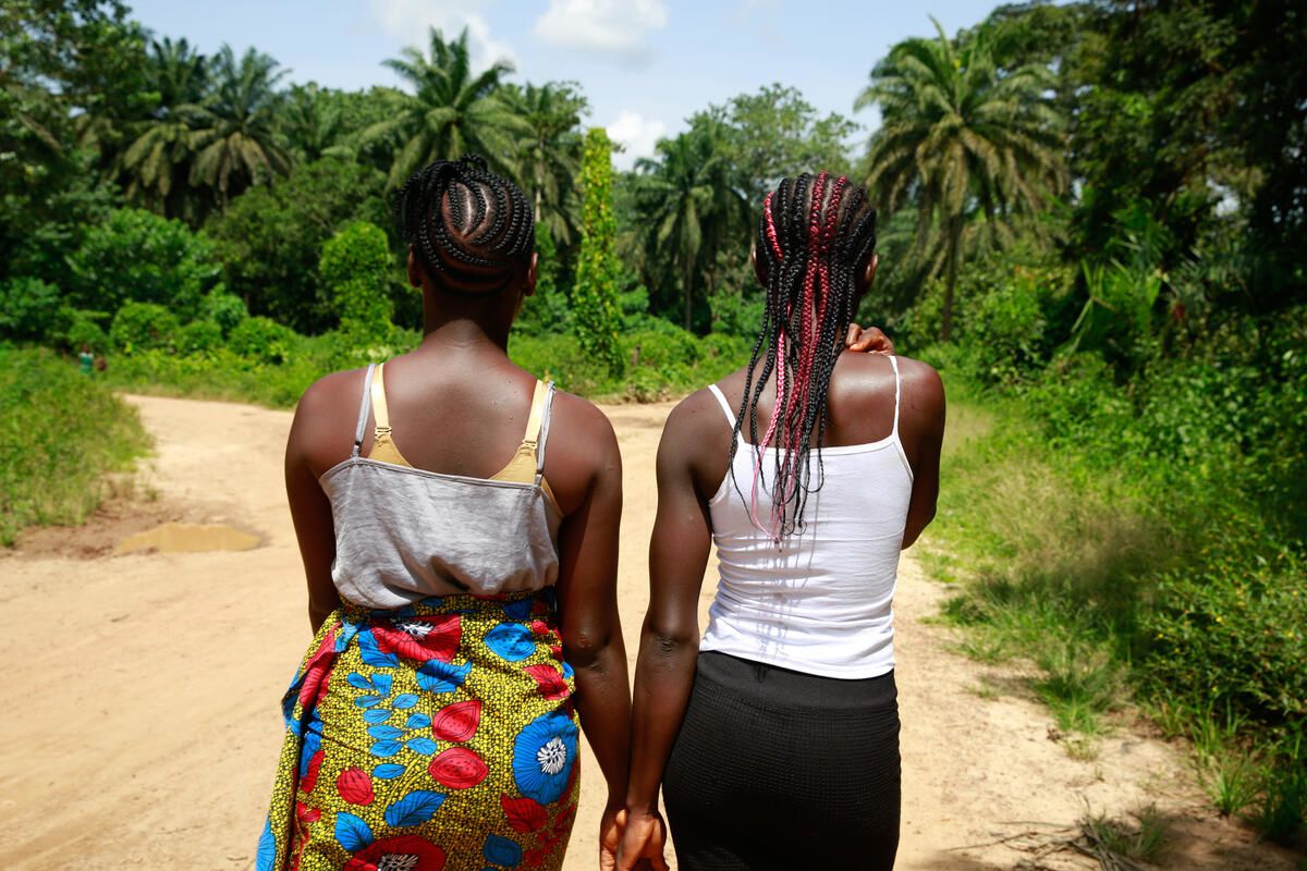 Cousins Kpemeh*, 18 and Kuji*, 19 walk home hand in hand in Kailahun, Sierra Leone