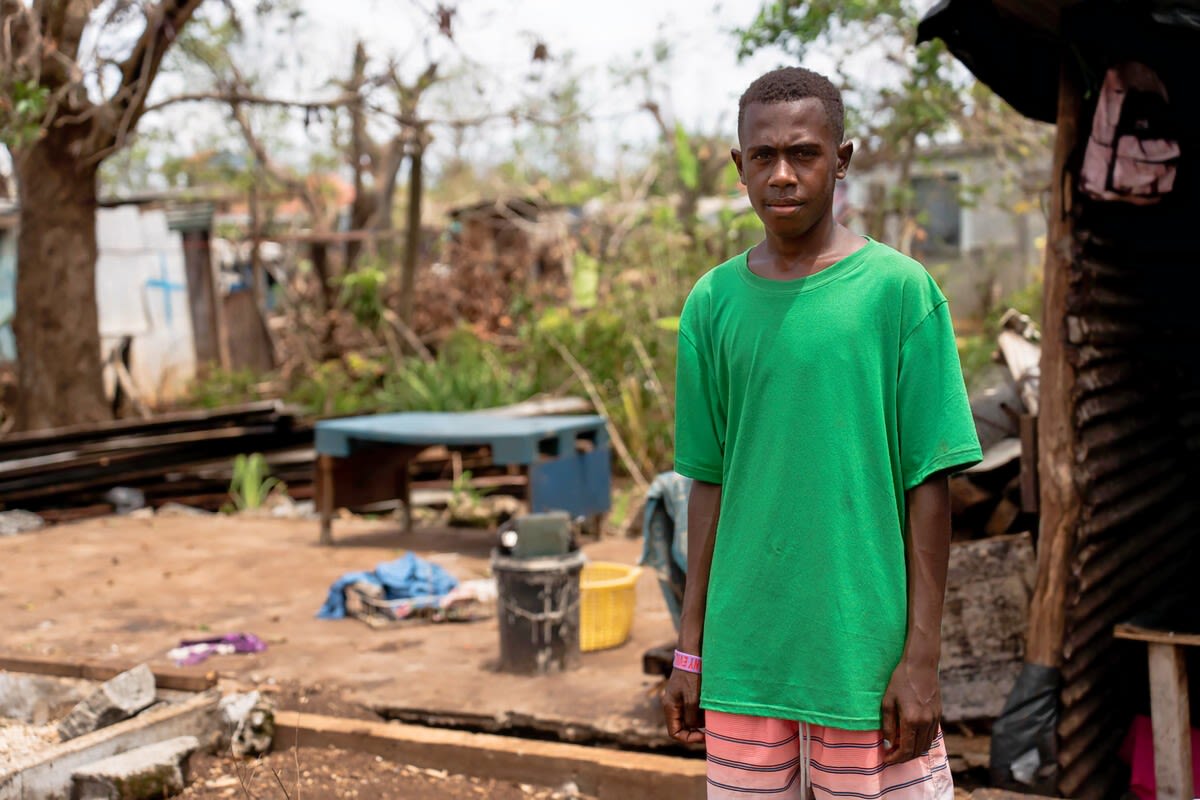 Lee Roy, a 15-year-old climate campaigner, in front of his family's house that was damaged during the tropical cyclones - Judy and Kevin - in Vanuatu