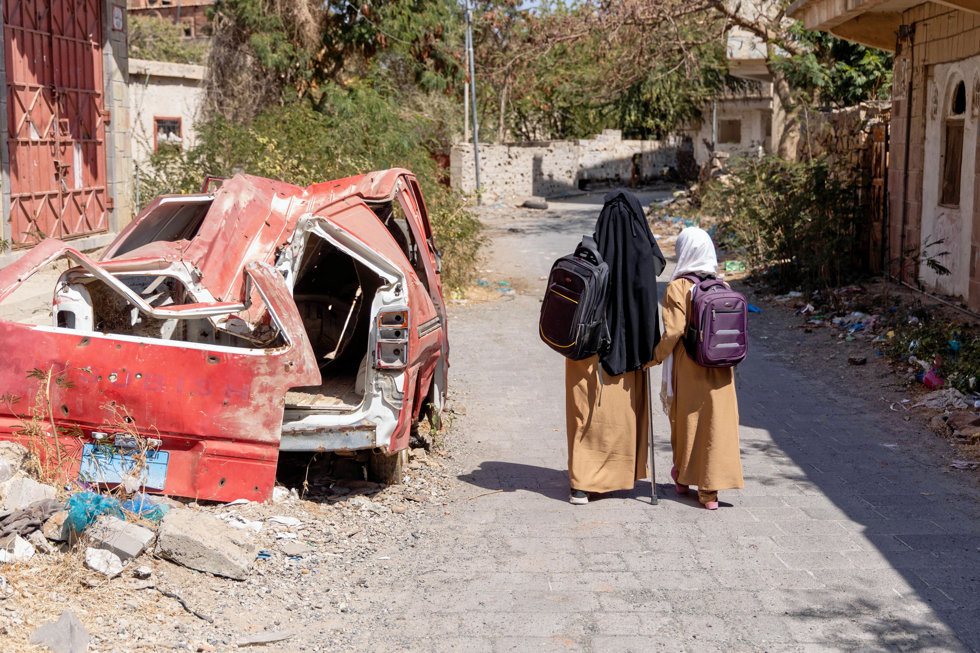 Two children walk home beside vehicle wreckage in Yemen
